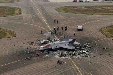 Wreckage of EA-18G Growler crash site on airport runway with emergency response personnel and vehicles present