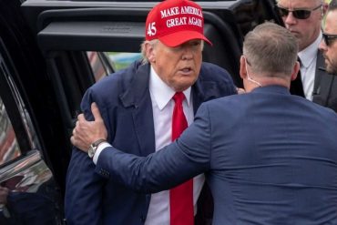 Political figure in red MAGA hat surrounded by security detail near vehicle, illustrating Donald Trump misinformation coverage