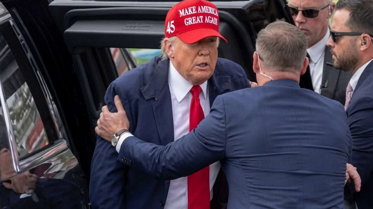Political figure in red MAGA hat surrounded by security detail near vehicle, illustrating Donald Trump misinformation coverage